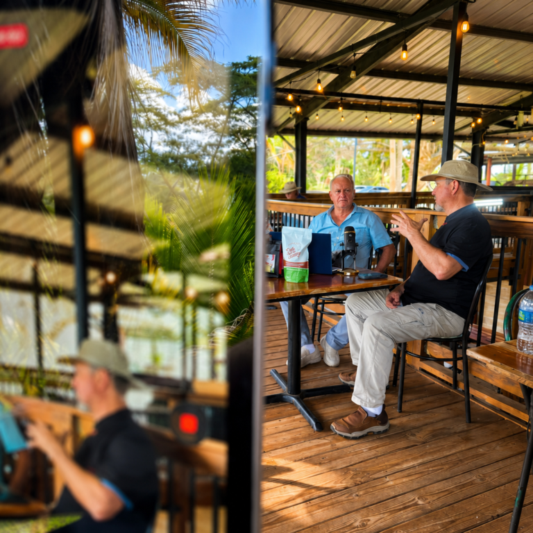Conversación en formato entrevista o podcast en un espacio tropical, capturada desde una perspectiva creativa con un celular en primer plano.